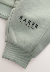 Hele-roheline dressipluusi varrukas soonikkoes mansetiga ja musta teksti "BAKER BY TED BAKER" trükk kangal.