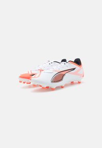 White soccer cleats with orange accents, textured synthetic upper, black detailing, and raised orange studs on a flat outsole.