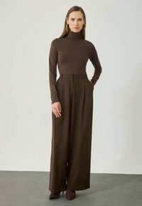 Blusa de gola alta castanha combinada com calças largas de cintura alta em castanho mais escuro. As calças apresentam pregas frontais e bolsos.