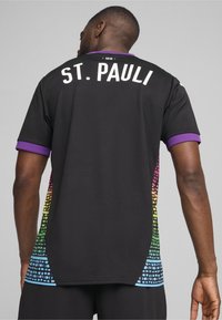 Camisa deportiva negra con cuello morado, con "ST. PAULI" en blanco en la parte posterior y un degradado multicolor y estampado en los laterales.
