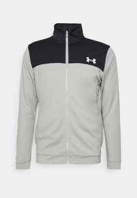 Veste zippée gris clair avec un panneau noir sur le haut de la poitrine et un col, avec un logo Under Armour blanc sur le côté gauche de la poitrine.
