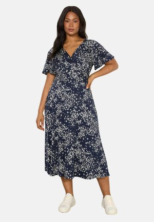 Marineblaues Blumen-Wickelkleid mit kurzen, flatternden Ärmeln, knielang, mit einem weißen Blumenmuster und einer fließenden Silhouette, kombiniert mit weißen Sneakers.