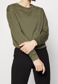 Olive green sweatshirt with a round neck, long sleeves, and ribbed cuffs; paired with black leggings, textured fabric.