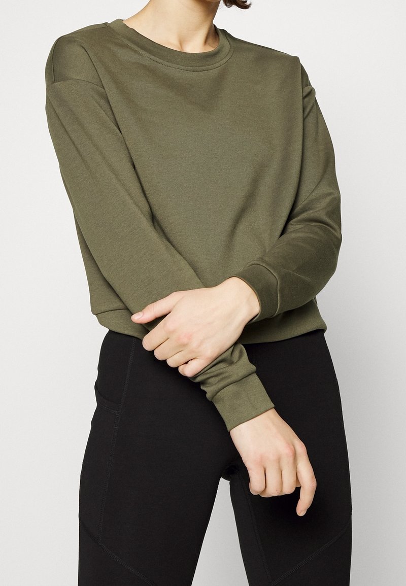 Olive green sweatshirt with a round neck, long sleeves, and ribbed cuffs; paired with black leggings, textured fabric.
