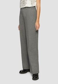 Pantalons à jambes larges en tissu gris doux, présentant un design ajusté avec une coupe droite et une texture subtile. Associés à des chaussures noires à lacets.