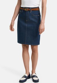 Gonna di jeans blu scuro, lunga fino al ginocchio, con una cintura marrone, cinque tasche e dettagli di cucitura in evidenza. Abbinata a mocassini bicolore.