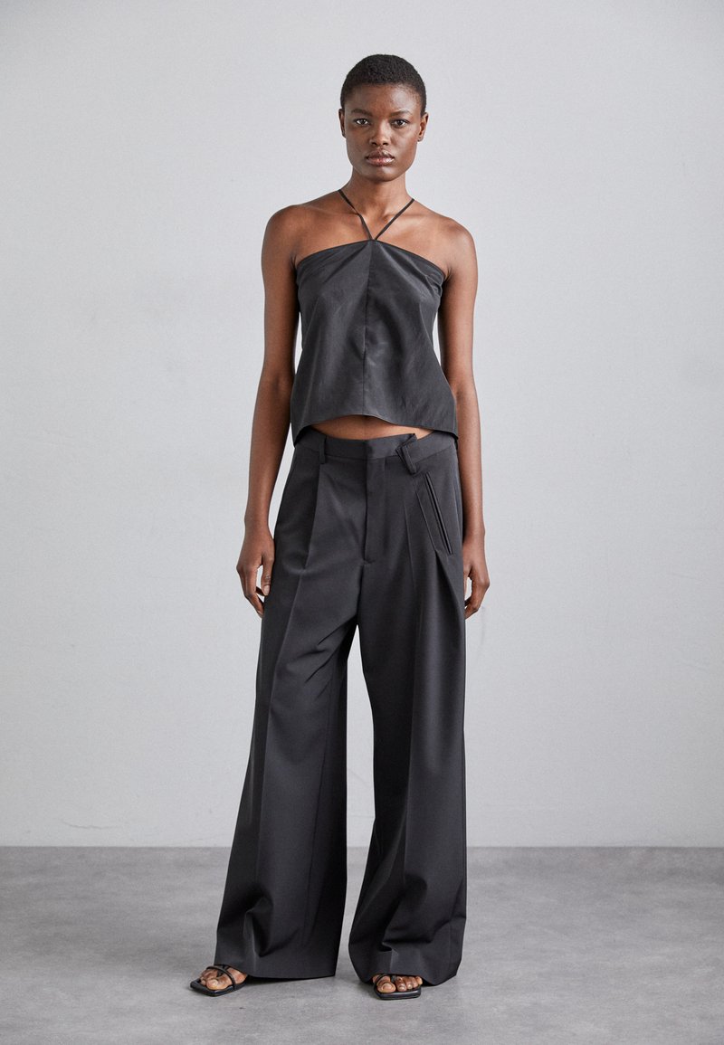 Black leather camisole with a relaxed fit and thin straps, paired with wide-leg black trousers featuring front pleats and a pocket detail.