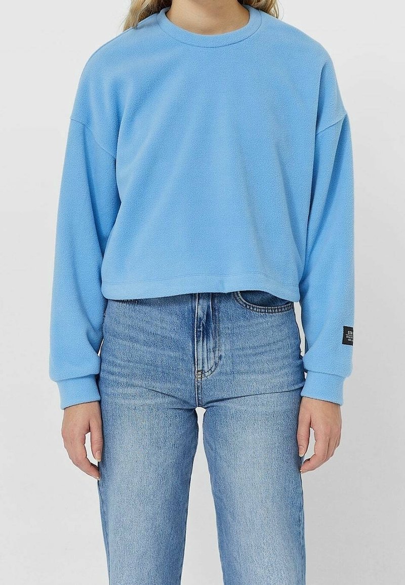 Felpa blu in pile con design corto, scollo rotondo e spalle scese, abbinata a jeans in denim azzurro a vita alta.