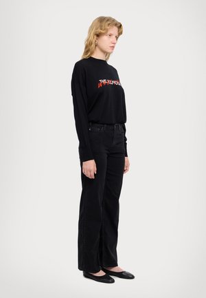 Black long-sleeve shirt with red graphic text, paired with high-waisted black jeans and black flats, featuring a relaxed fit and soft texture.