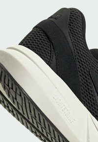 Čierne atletické topánky s textúrovaným sieťovinovým zvrškom a hladkými detailmi. Biela medzipodrážka s gravírovaným nápisom "LIGHTSTRIKE" a vzorovaná gumová podrážka.