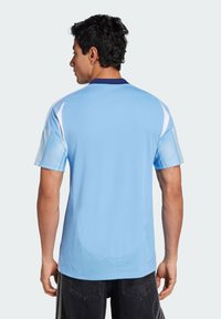 Jersey deportivo azul claro con mangas cortas, que presenta paneles laterales blancos y un cuello navy. Textura suave con un dobladillo redondeado.