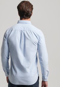 Lichtblauw overhemd met lange mouwen en een button-down kraag. Zachte textuur, rechte snit en een rugplooi voor meer bewegingsvrijheid.
