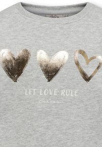Grå sweatshirt med tre hjärtan i guldfolie ovanför texten "LÅT KÄRLEKEN REGERA" i vitt, med en avslappnad rund halsringning och mjuk textur.