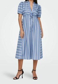 Ljusblå, knälång klänning med vertikala vita ränder, korta puffärmar, djup V-ringning och knytning i midjan. I kombination med svarta sandaler.