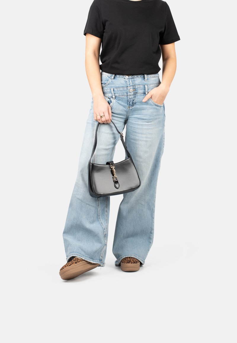 Sac en cuir noir avec une forme structurée et des garnitures dorées, associé à un jean bleu clair à jambes larges et des chaussures à enfiler en imprimé animal.