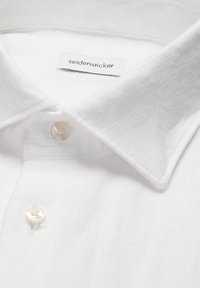 Col de chemise blanche avec deux boutons en perle et une étiquette de marque "seidensticker" visible à l'intérieur de l'encolure.