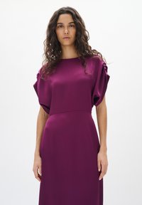 Robe violette avec des manches courtes et bouffantes et une silhouette droite. Fabriquée en tissu texturé, avec une finition lisse et des coutures subtiles.