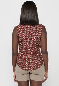 Blusa sin mangas con un patrón floral de color rojo oscuro, que presenta pequeñas flores blancas y rosas. Tejido suave, dobladillo redondeado y diseño ajustado.