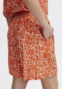 Korte broek van lichtgewicht stof met een oranje en crèmekleurig bloemmotief, voorzien van een elastische tailleband en zijzakken.