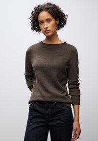 Brauner Strickpullover mit rundem Halsausschnitt und langen Ärmeln, kombiniert mit dunkelb blauen Jeans. Dezente Textur, taillierte Passform und minimale Details.