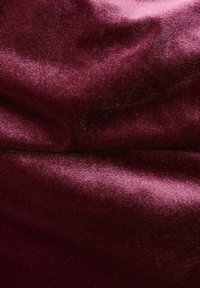 Burgundská sametová tkanina s hladkým povrchem a jemným leskem, která má mírné barevné a povrchové variace, což vytváří bohatý vzhled.