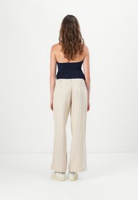 Pantalons en lin crème à coupe décontractée avec une taille élastique, associés à un haut smocké bleu marine. Texture lisse, design à jambe large.