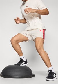 Μαύρος ελαστικός θόλος ισορροπίας με ένα άτομο που φοράει ανοιχτό μπεζ πουκάμισο και σορτς με κόκκινες ρίγες, και μαύρα αθλητικά παπούτσια.