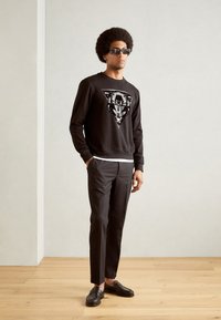 Sudadera negra con un diseño gráfico de pantera, combinada con pantalones ajustados negros y mocasines negros, todo sobre un fondo neutro.