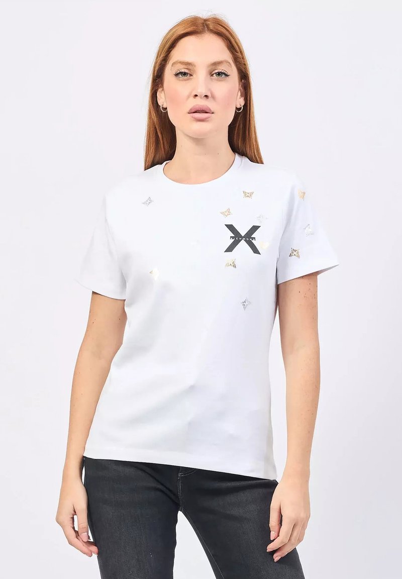 T-shirt bianco a maniche corte con diversi motivi a stella metallici e un logo "X" nero sul fronte. Materiale in cotone morbido.
