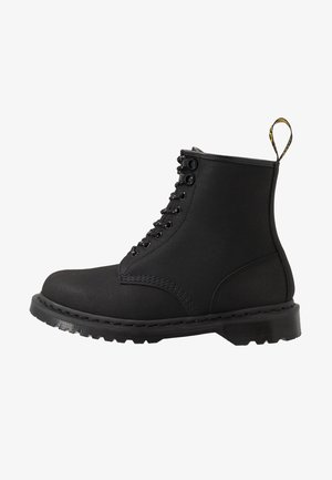 Bottes noires à lacets avec une surface en toile lisse, bout rond, semelle en caoutchouc et une languette au talon. Détails cousus visibles.