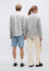 Ριγέ πουκάμισα με κουμπιά και μακριά μανίκια· το ένα συνδυασμένο με τζιν σορτς, το άλλο με κρεμ παντελόνια με φιόγκο διακοσμήσεις.