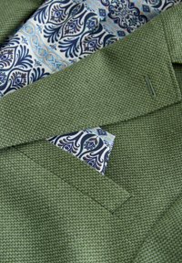 Groene blazer met een textuur, mouw zichtbaar met een blauw-wit patroon pochet en een bijpassende overhemdmanchet.