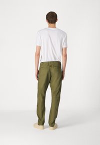 Olieti zaļas kravas bikses ar vairākiem kabatām, taisnu kāju dizainu un izturīgu audumu. Valkātas ar vienkāršu balto t-kreklu un gaišām kurpēm.