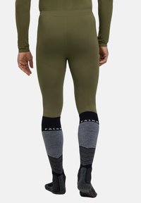 Leggings ajustés vert olive avec un design texturé, associés à des chaussettes grises mi-mollet avec des accents noirs et des détails de marque.