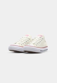 Canvas low-top sneakers in off-white with pink brand tag and gray-blue accents. Features round laces, metal eyelets, and rubber sole.