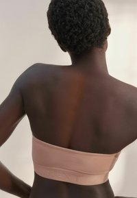 Lichtroze strapless bralette gemaakt van rekbaar materiaal, met een zachte textuur en een gemerkte elastische band rond de onderkant.