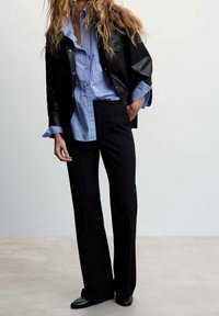 Musta nahkatakki vaalean sinisen raidallisen paidan päällä, yhdistettynä mustiin leveälahkeisiin housuihin ja mustiin kenkiin. Yksinkertainen ja moderni muotoilu.