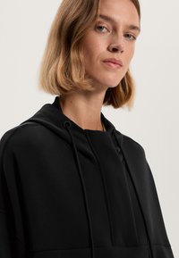 Felpa nera con cappuccio e vestibilità comoda, dotata di tasca a marsupio, lacci regolabili e una texture di tessuto liscia.