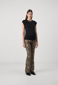 Camisa negra de manga corta combinada con pantalones acampanados fluidos y estampados en rayas de cebra en tonos beige y negro. La modelo lleva calzado negro de punta.