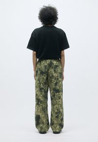 Zwarte katoenen T-shirt, relaxte pasvorm, gecombineerd met groene cargo-broek met een patroon in gedempte aardetinten en een brede, relaxte silhouet.