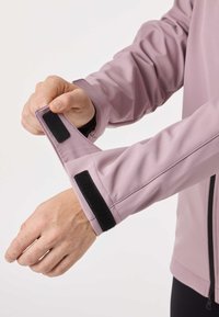 Hands adjusting black Velcro strap on lavender jacket sleeve against a plain light background.