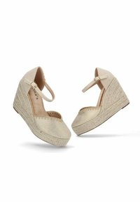 Zapatos de cuña en color beige con textura tejida, correa en el tobillo y punta redondeada. Cuenta con una suela de yute trenzado para un detalle adicional.