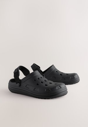 Schwarze wasserdichte Clogs aus Gummi mit verstellbarem Fersenriemen, Belüftungsöffnungen, strukturiertem Sohlenprofil und geformtem Design.