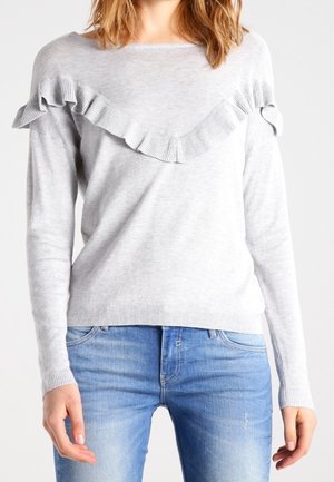 Lichtgrijze trui met een geribbelde halssluiting en een decoratieve ruches aan de voorkant. Zachte textuur met een relaxte pasvorm, gecombineerd met blauwe jeans.