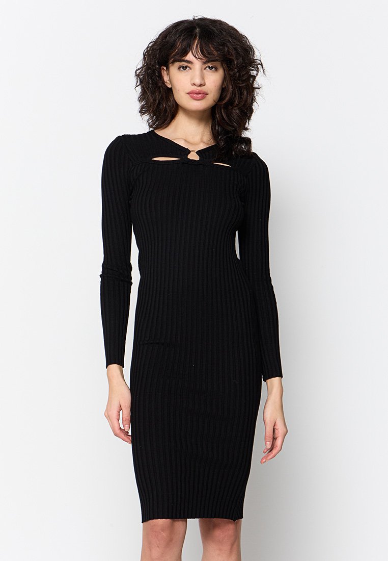 Vestido de punto negro con costura acanalada y mangas largas, con escote redondo y dos detalles cortados en el pecho. Silueta ajustada.