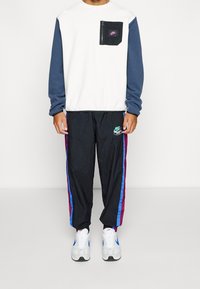 Vit och marinblå långärmad sweatshirt med dragkedjeficka; svarta, lätta löparbyxor med blå och vinröd sidostrimma; vita och blå sneakers.