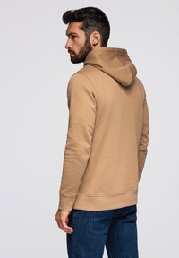 Hnědá mikina s klokaní kapsou, žebrovanými manžetami a lemem a kapucí se stahovací šňůrkou, kombinovaná s modrými džínami. Hladká textura a ležérní design.