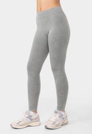 Gray leggings made of soft, stretchy fabric; high waistband; smooth texture; paired with light gray and beige athletic shoes.
