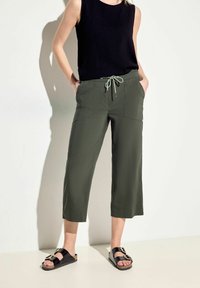 Culottes vert olive avec une taille à cordon, deux poches avant et une coupe décontractée, accompagnés d'un haut sans manches noir et de sandales noires.