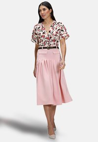 Blouse florale à manches courtes en blanc et rose, associée à une jupe plissée rose de longueur moyenne. Comprend une ceinture noire.